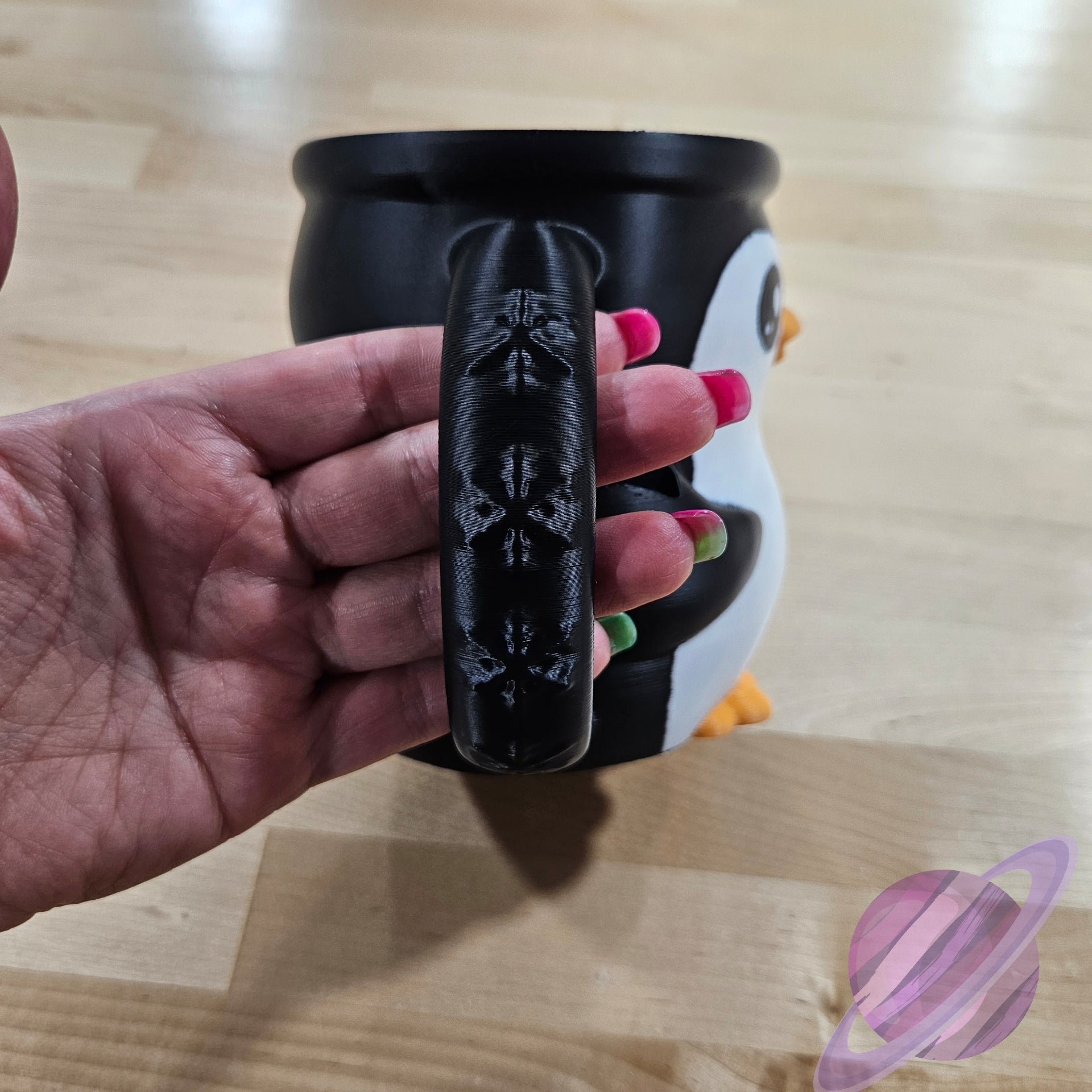 Hand holding a black mug handle with floral patterns on a wooden surface