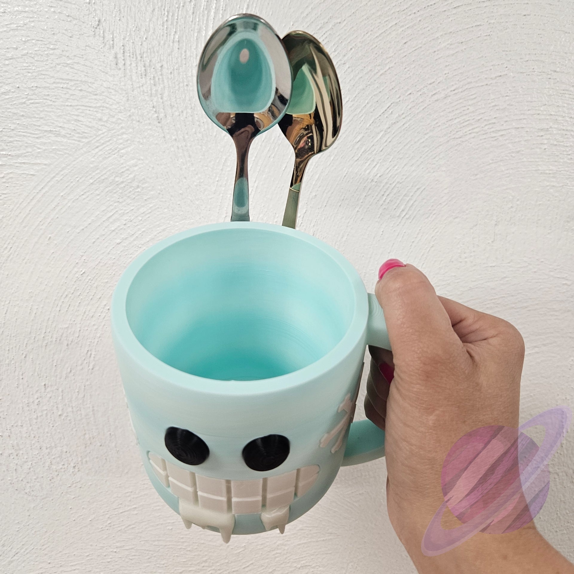 Blue mug with a face design holding two spoons against a white background