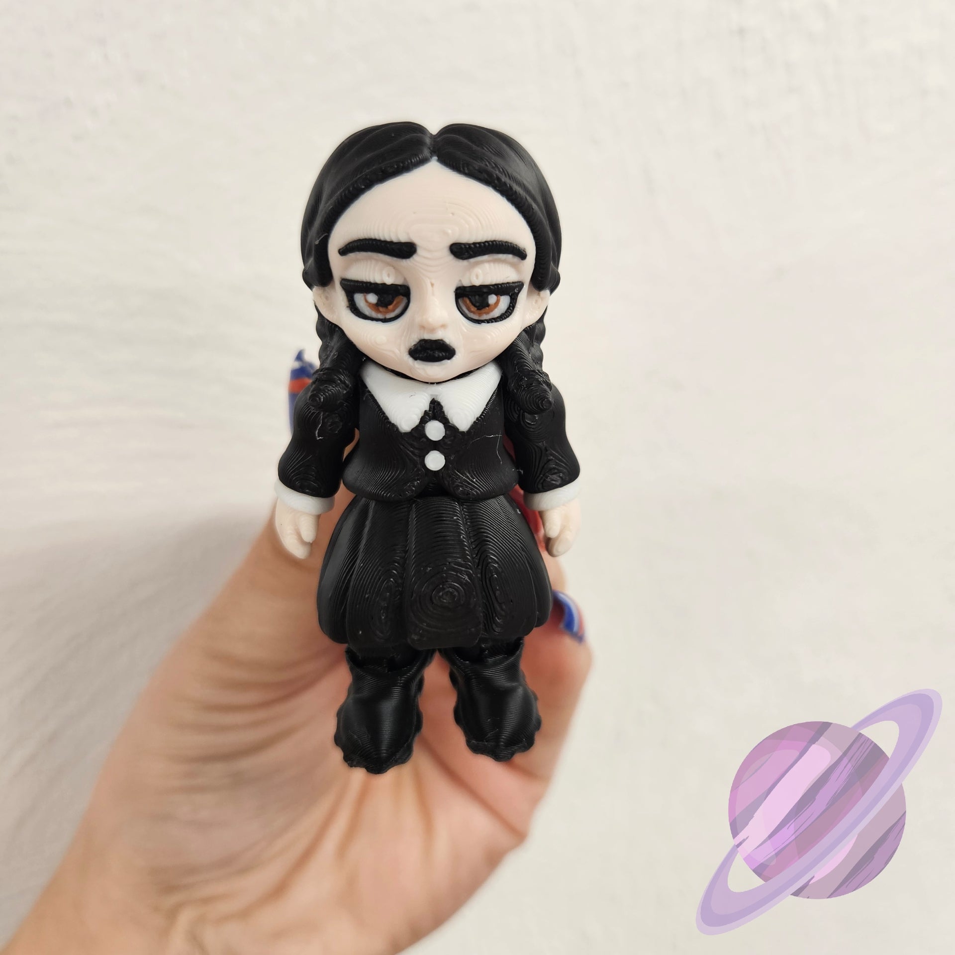 Toy figure of a character with black hair and clothing held in a hand against a light background