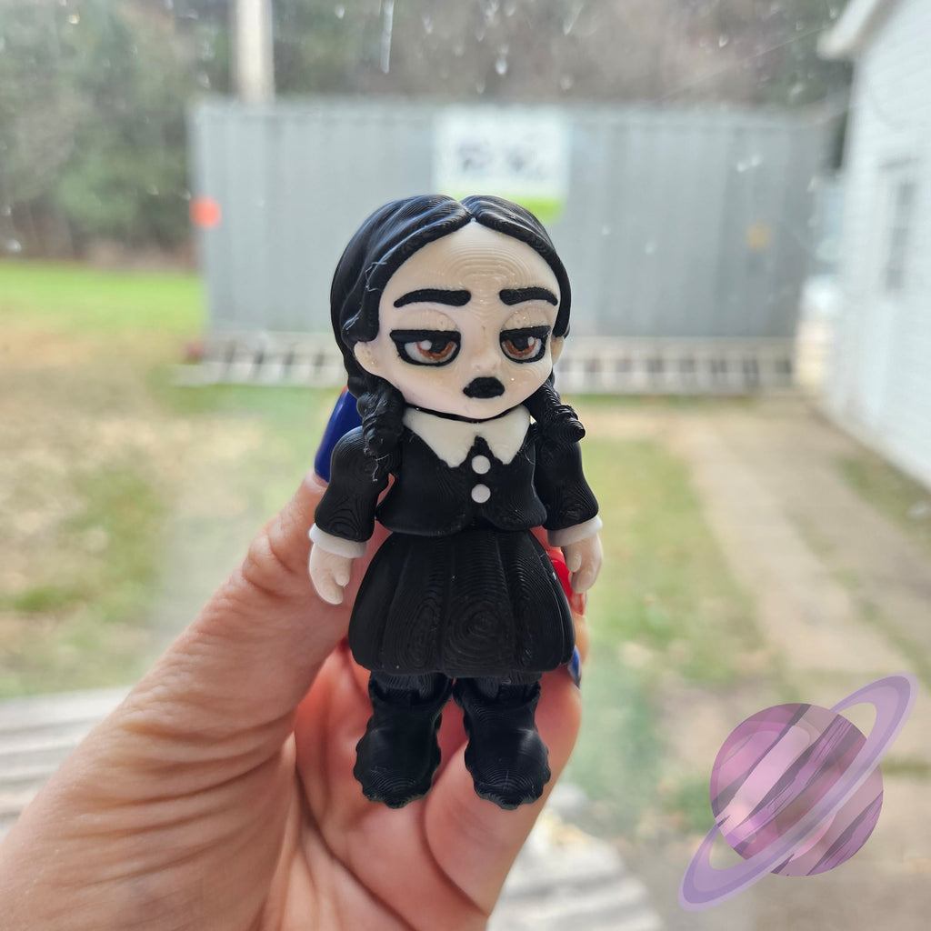 Hand holding a small figurine of a character with black hair and dress, outdoors.
