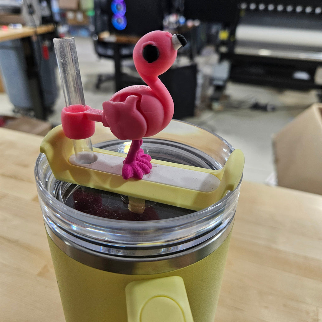 Yellow tumbler with a pink flamingo drink valve on a wooden surface.