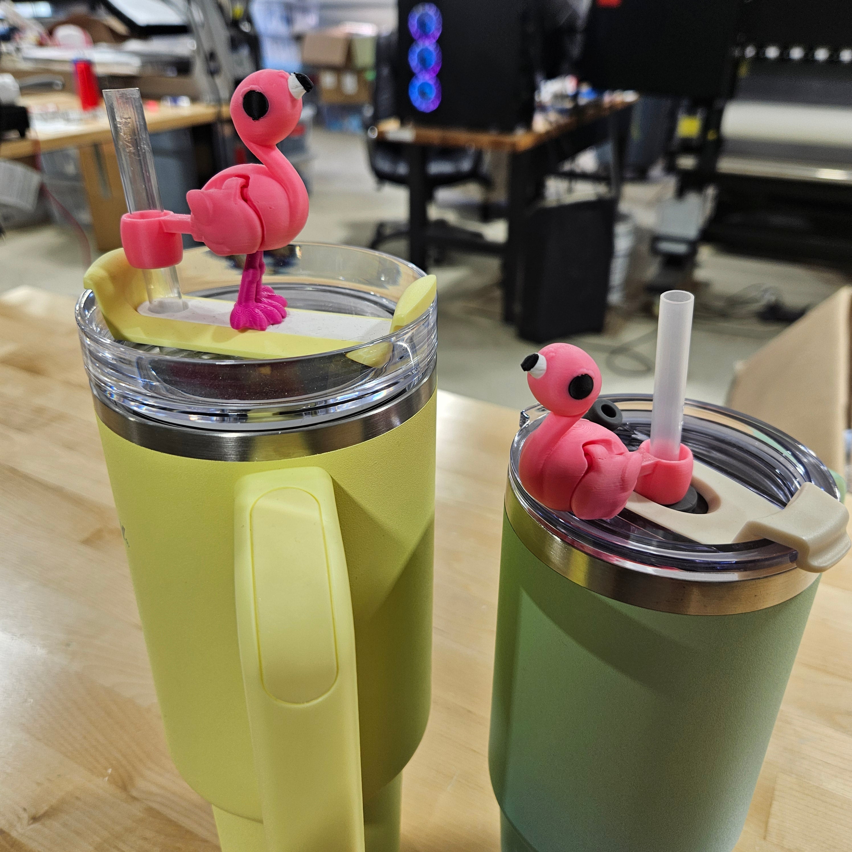 Two colorful tumblers with pink flamingo drink accessories on a wooden surface.