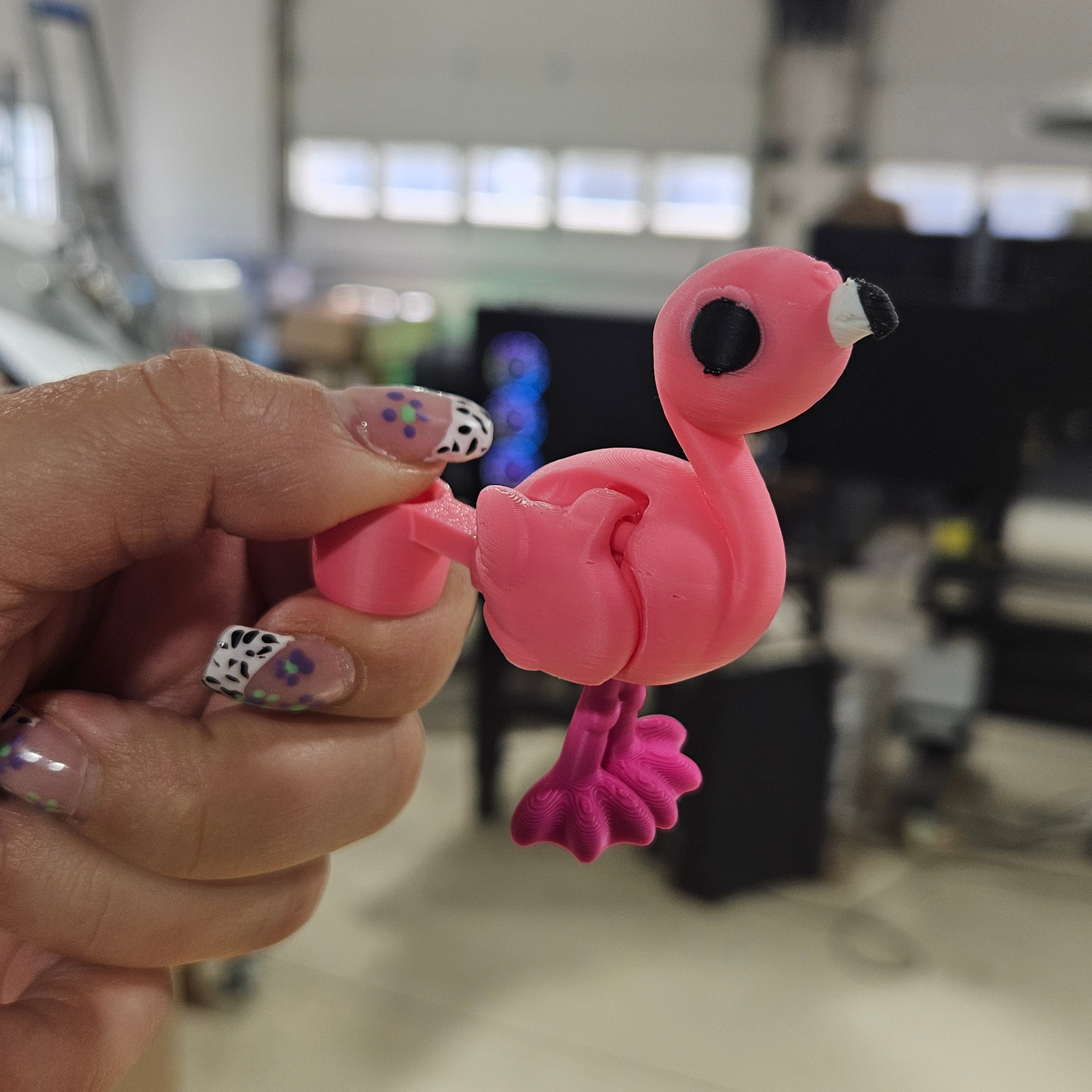 Pink flamingo-shaped object held by a hand with colorful nail polish in an indoor setting.