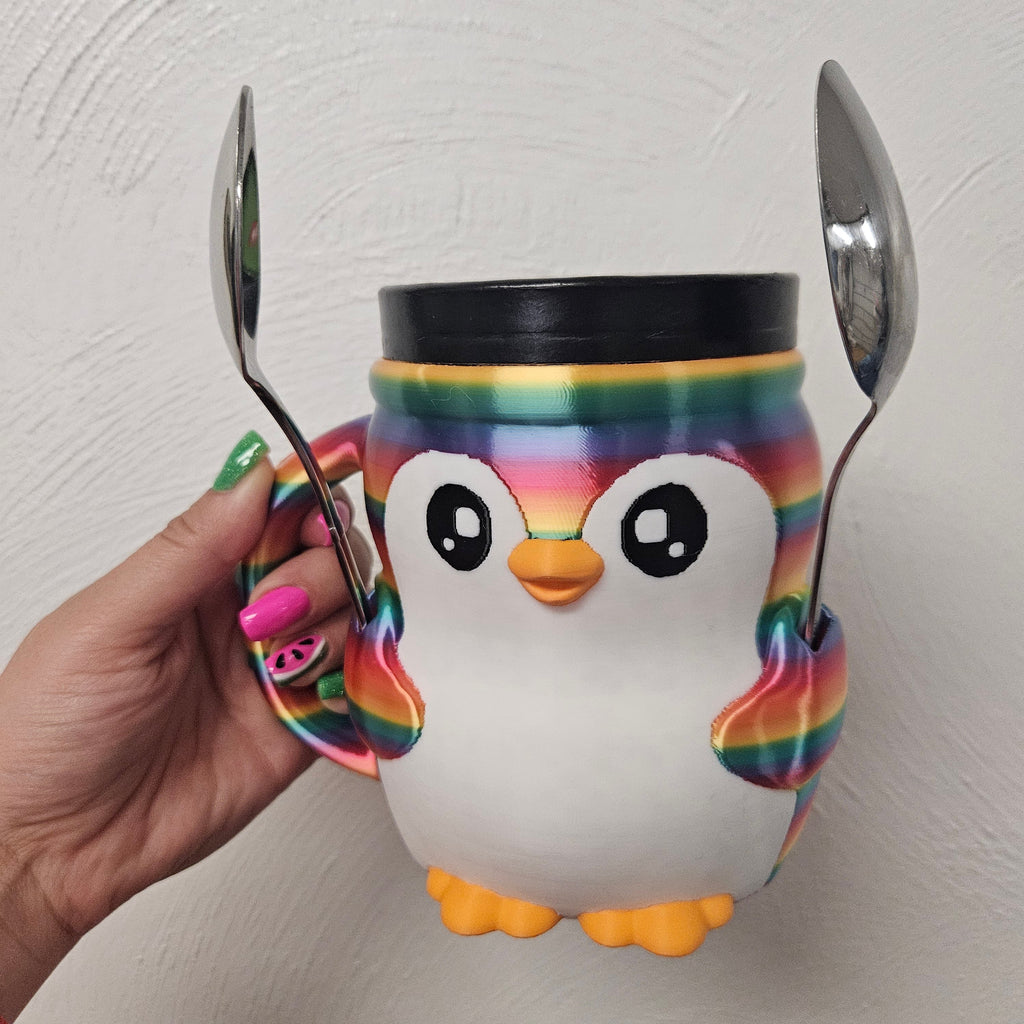 Colorful penguin mug with rainbow design held by a hand against a light background