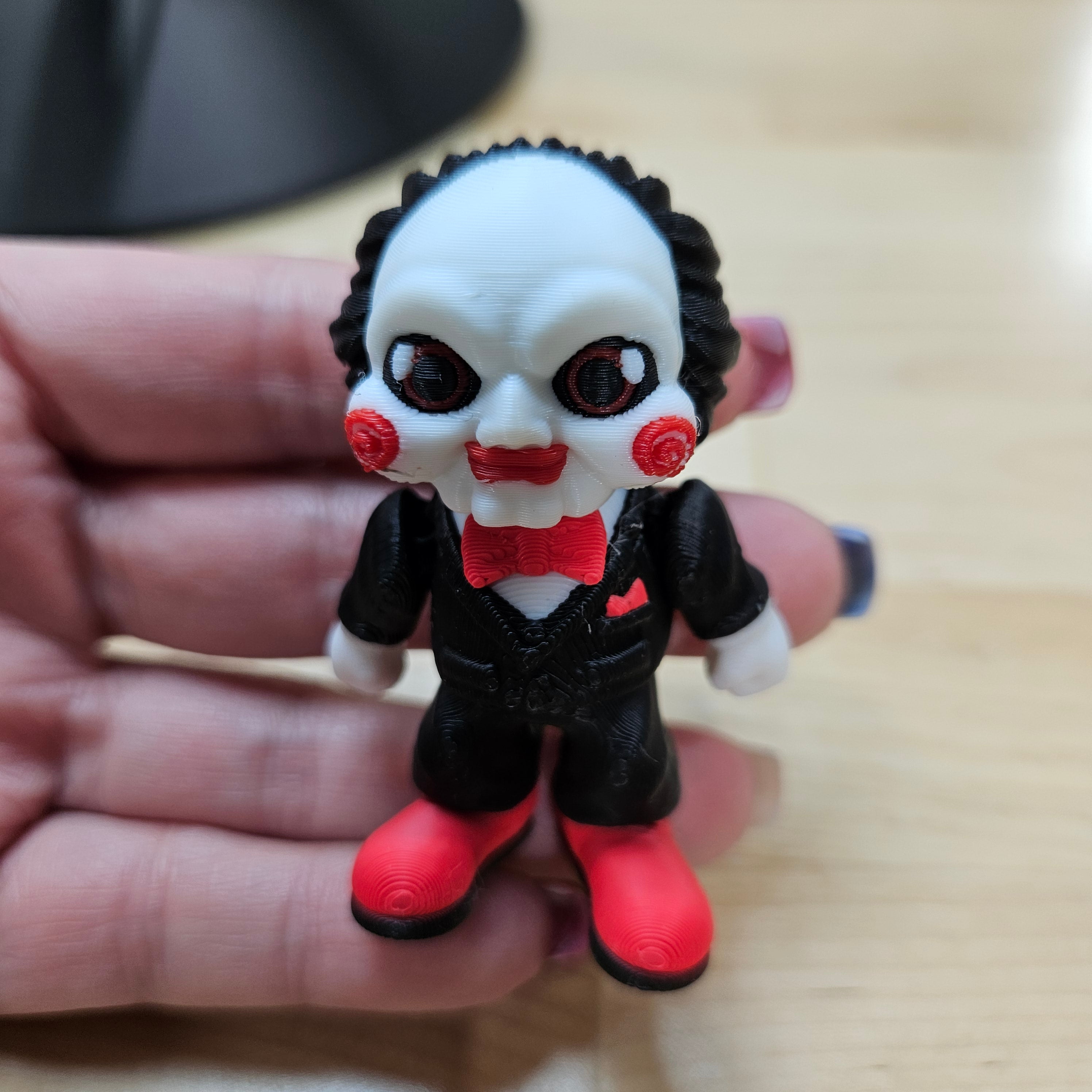 Toy figure with black hair, red eyes, and a red bow tie held in a hand.