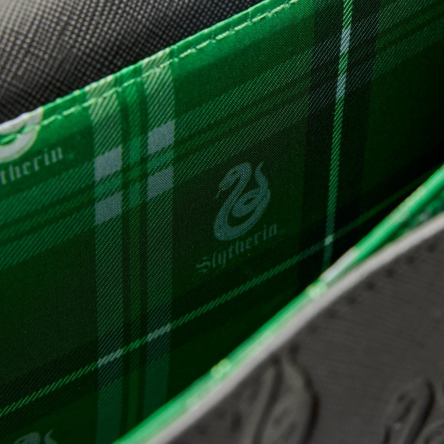 Close-up of a green plaid fabric with 'Slytherin' branding on a black background.