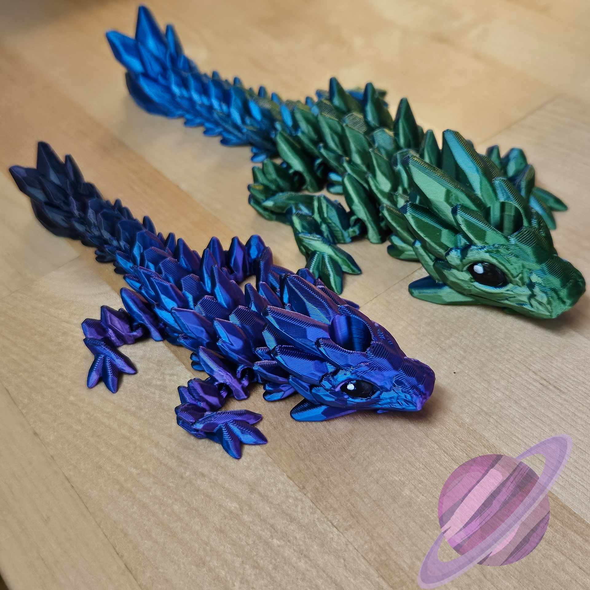 Two 3D-printed dragon models, one blue and one green, on a wooden surface.