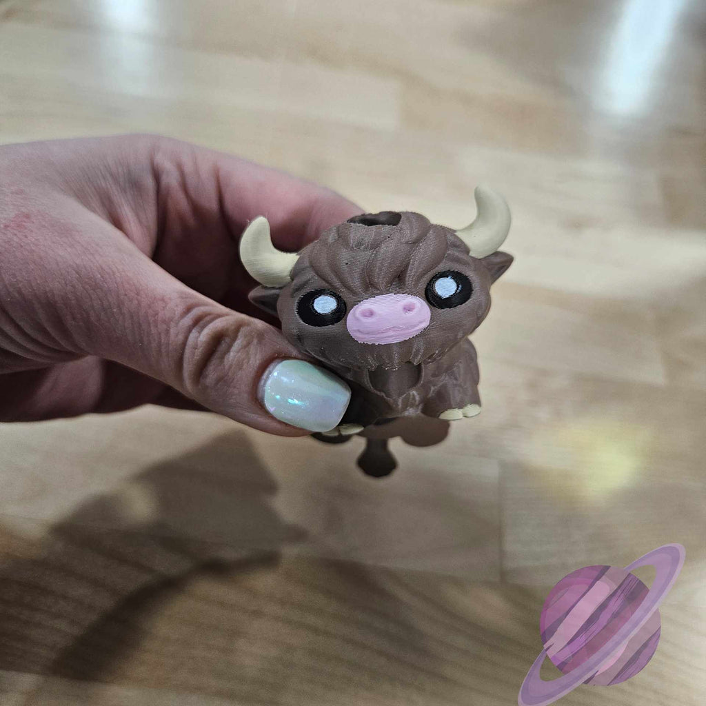 Hand holding a small brown animal figurine with white horns on a wooden surface