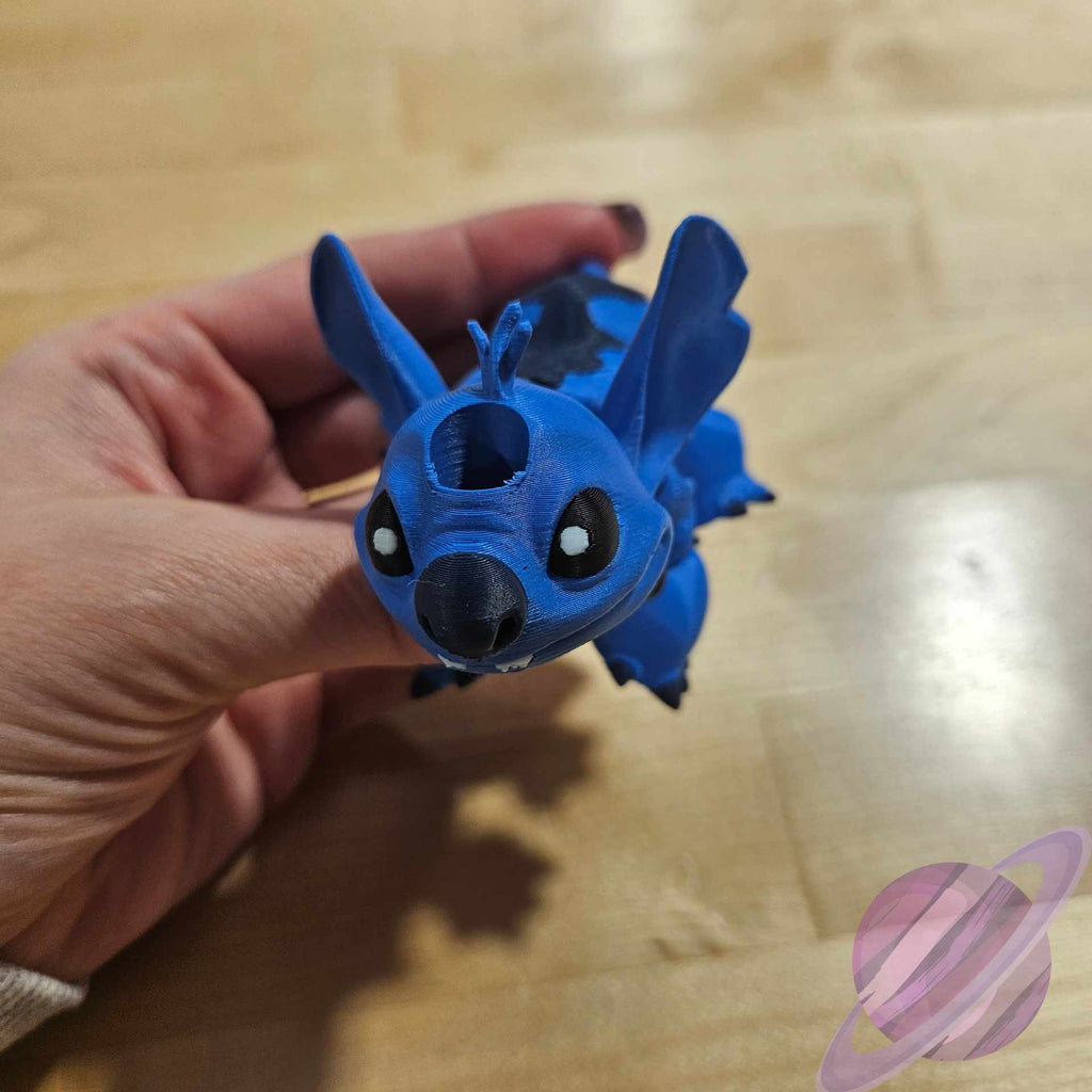 Blue plush toy resembling a dragon held by a hand on a wooden surface