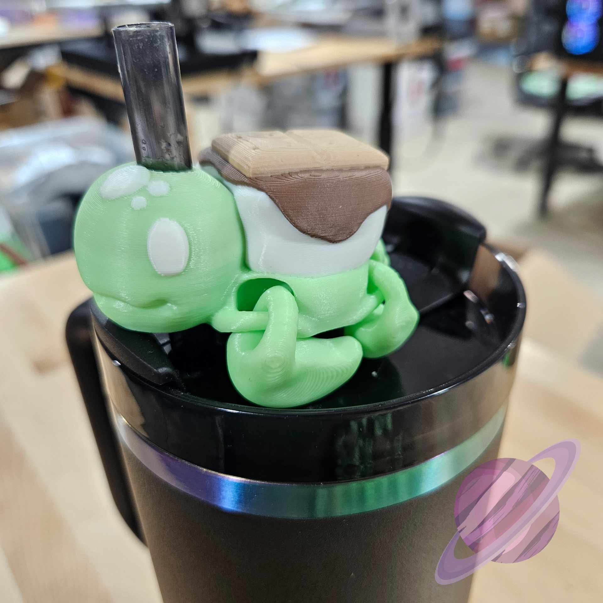 Green cartoon turtle figurine on top of a black container with a blurred indoor background