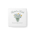 A square white ceramic coaster with rounded corners featuring a floral bouquet illustration and the text 'Rooted in Faith' and 'Blooming through motherhood'.