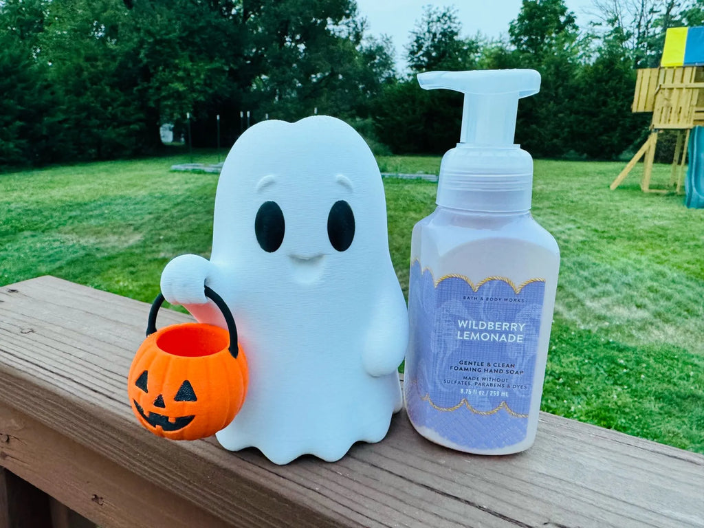 A white ghost-shaped container holding an orange pumpkin bucket sits next to a pump bottle labeled Wildberry Lemonade on a wooden deck with a grassy backyard in the background.