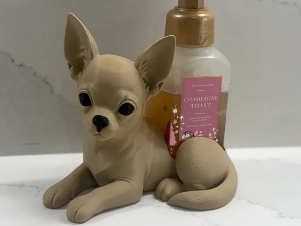 A beige ceramic figurine of a Chihuahua dog positioned in front of a pump bottle of Bath & Body Works 'Champagne Toast' scented lotion on a white marble surface.