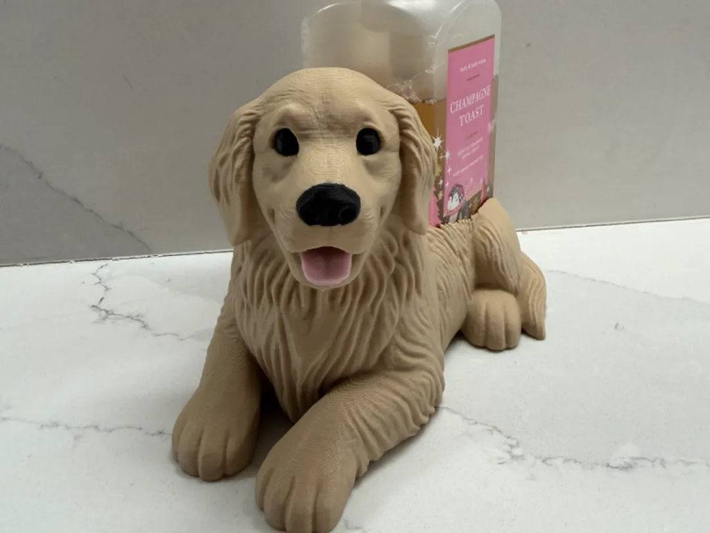 A beige rubber dog toy shaped like a golden retriever lying down, positioned in front of a pink-labeled bottle on a white marble-patterned surface.