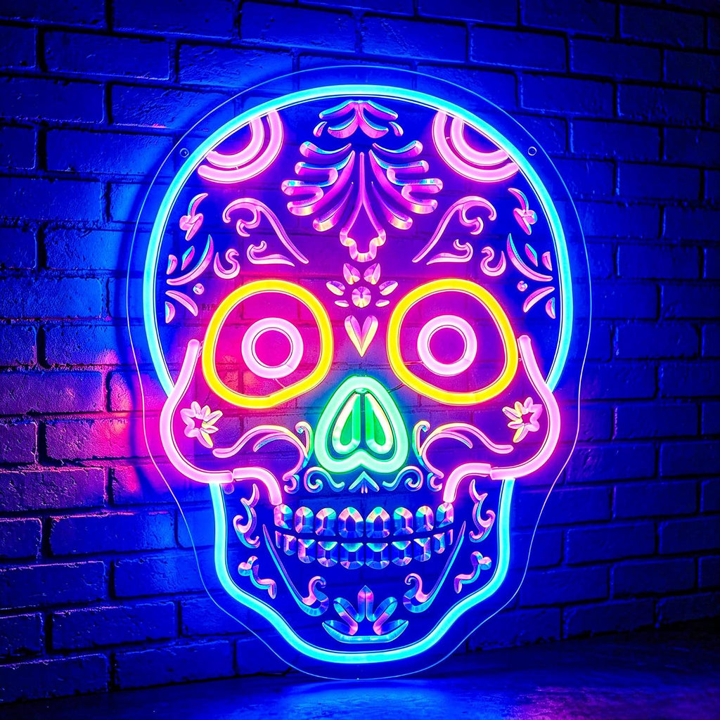 A colorful neon skull sign with intricate Day of the Dead style floral detailing, glowing in vibrant pink, blue, yellow, green, and purple tones against a dark blue brick wall.