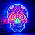 A colorful neon skull sign with intricate Day of the Dead style floral detailing, glowing in vibrant pink, blue, yellow, green, and purple tones against a dark blue brick wall.