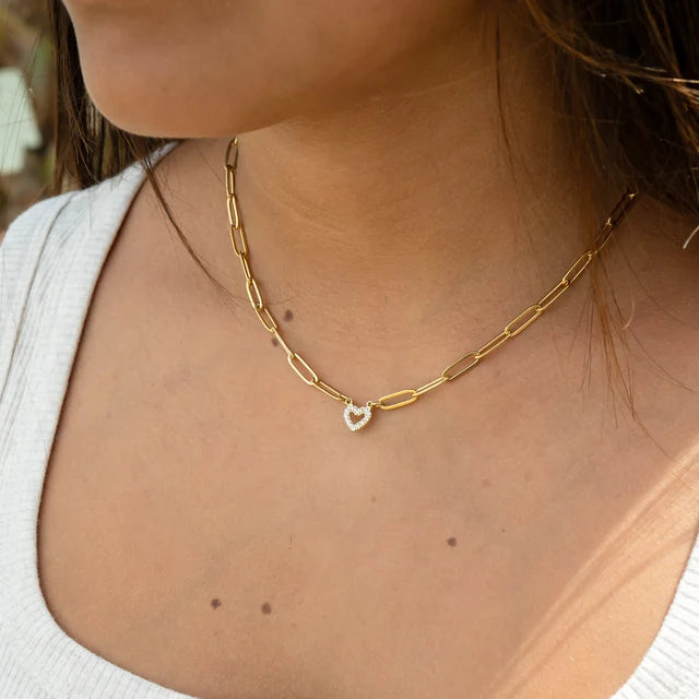 Gold chain necklace with a heart pendant on a person wearing a white top.