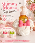 A white faux-fur styled mouse-head shaped soap holder with a large pink bow, shown holding a foaming hand soap bottle. The image includes promotional text reading 'Mummy Mouse Soap Holder,' icons noting foamable hand soap bottle fit and bow color options, and small product variants with pink and green bows.