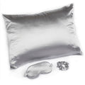Silver satin pillow, eye mask, and scrunchie on a white background