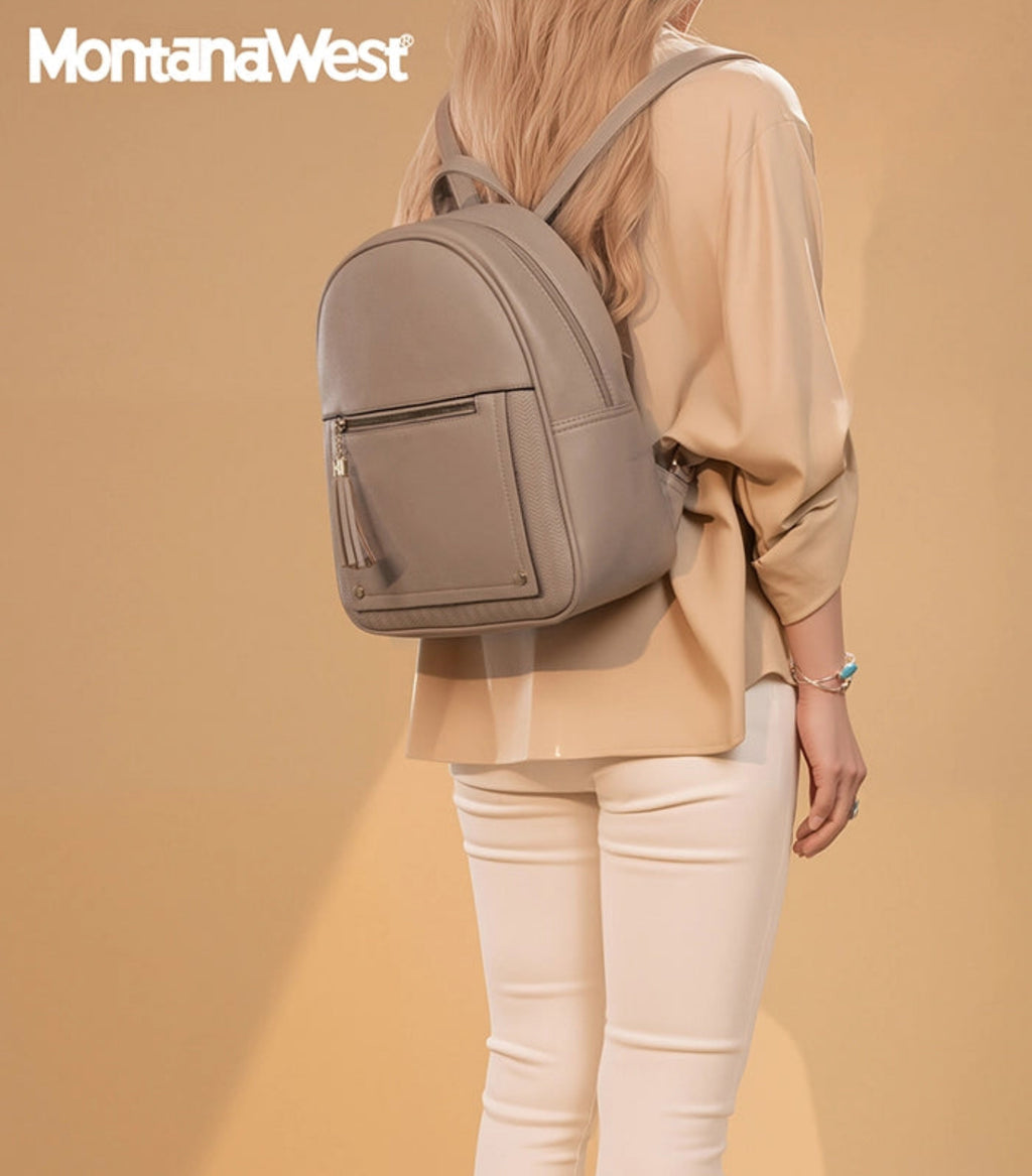 A woman shown from the back wearing a light taupe-gray backpack with a front zippered pocket and tassel detail, styled with a beige blouse and cream pants against a solid beige studio background. The Montana West brand logo is visible in the top left corner.