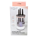 Estelle Beauty Sonic Brush Cleaner & Holder in its retail packaging, featuring a clear cylindrical container with four black bristles, a rose gold metallic collar, and a white base, shown on a white background.