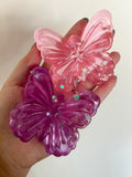 Pink and purple butterfly-shaped objects held in a hand against a light background