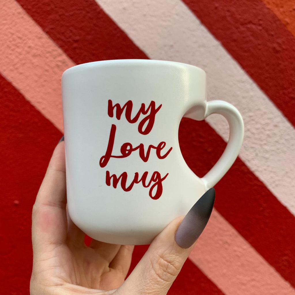 White mug with 'my love mug' text held against a red and orange striped background