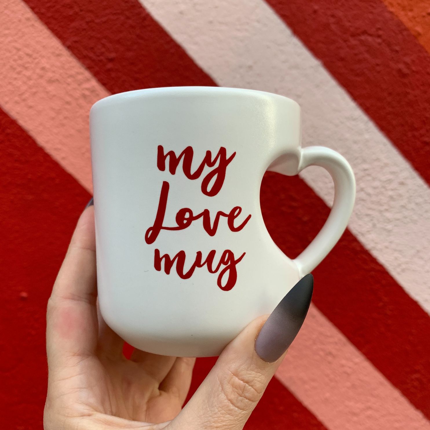 White mug with 'my love mug' text held against a red and orange striped background
