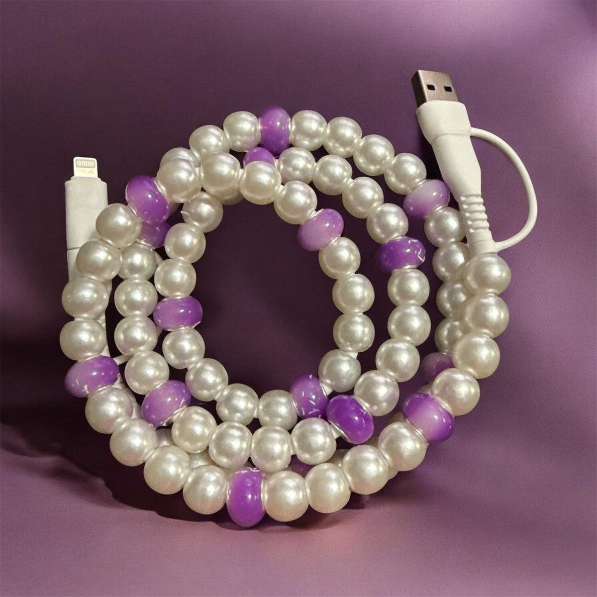 A coiled white faux-pearl USB cable with alternating translucent purple beads, shown on a purple gradient background.