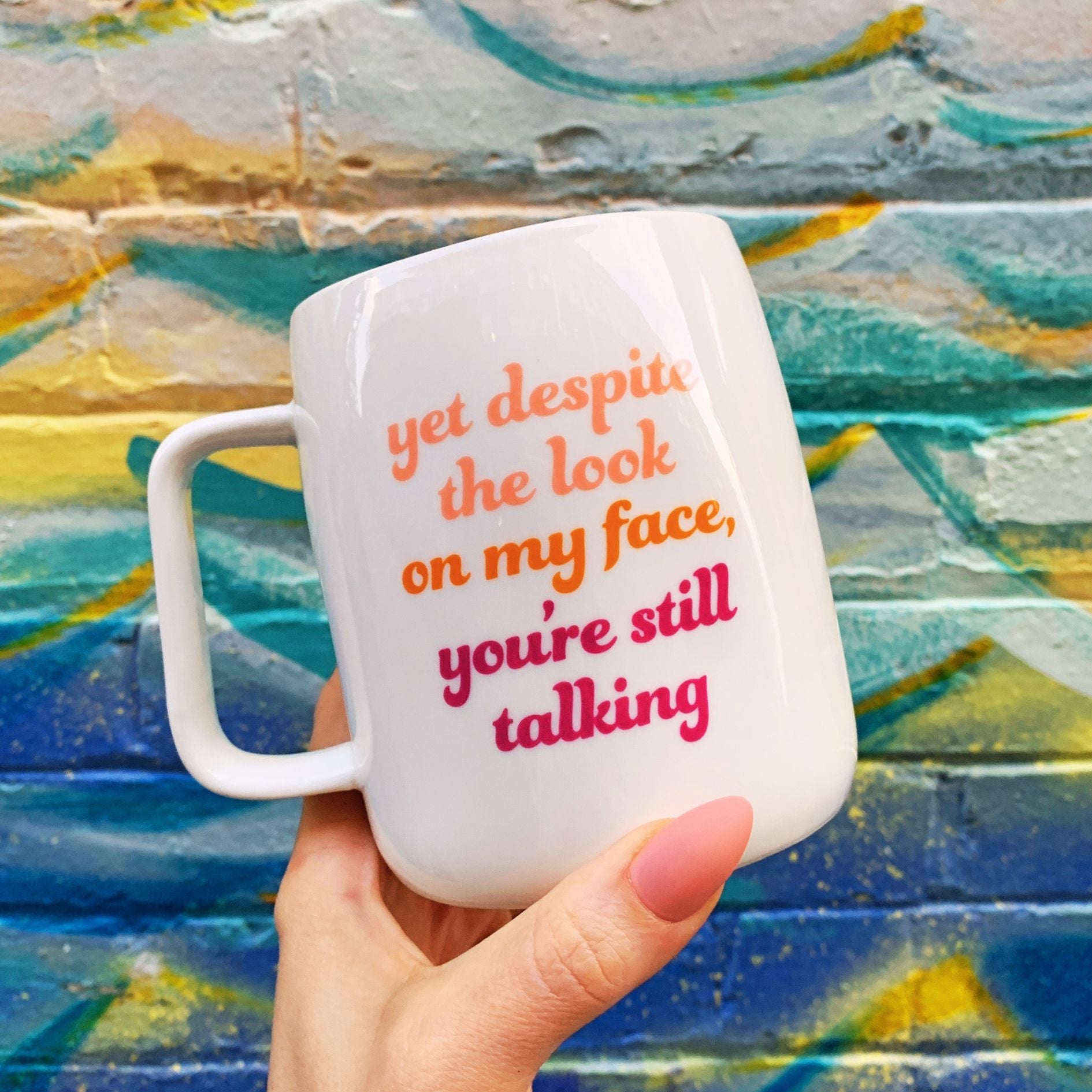 White mug with colorful text held in front of a colorful abstract painting