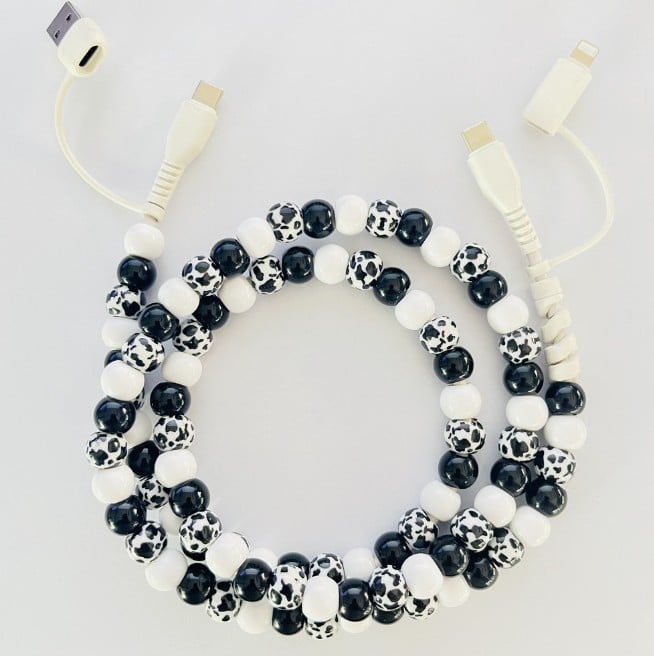 A coiled beaded phone cable with alternating black-and-white soccer ball patterned beads and solid white beads, featuring cream-colored USB-A and Lightning connectors on a light gray background.
